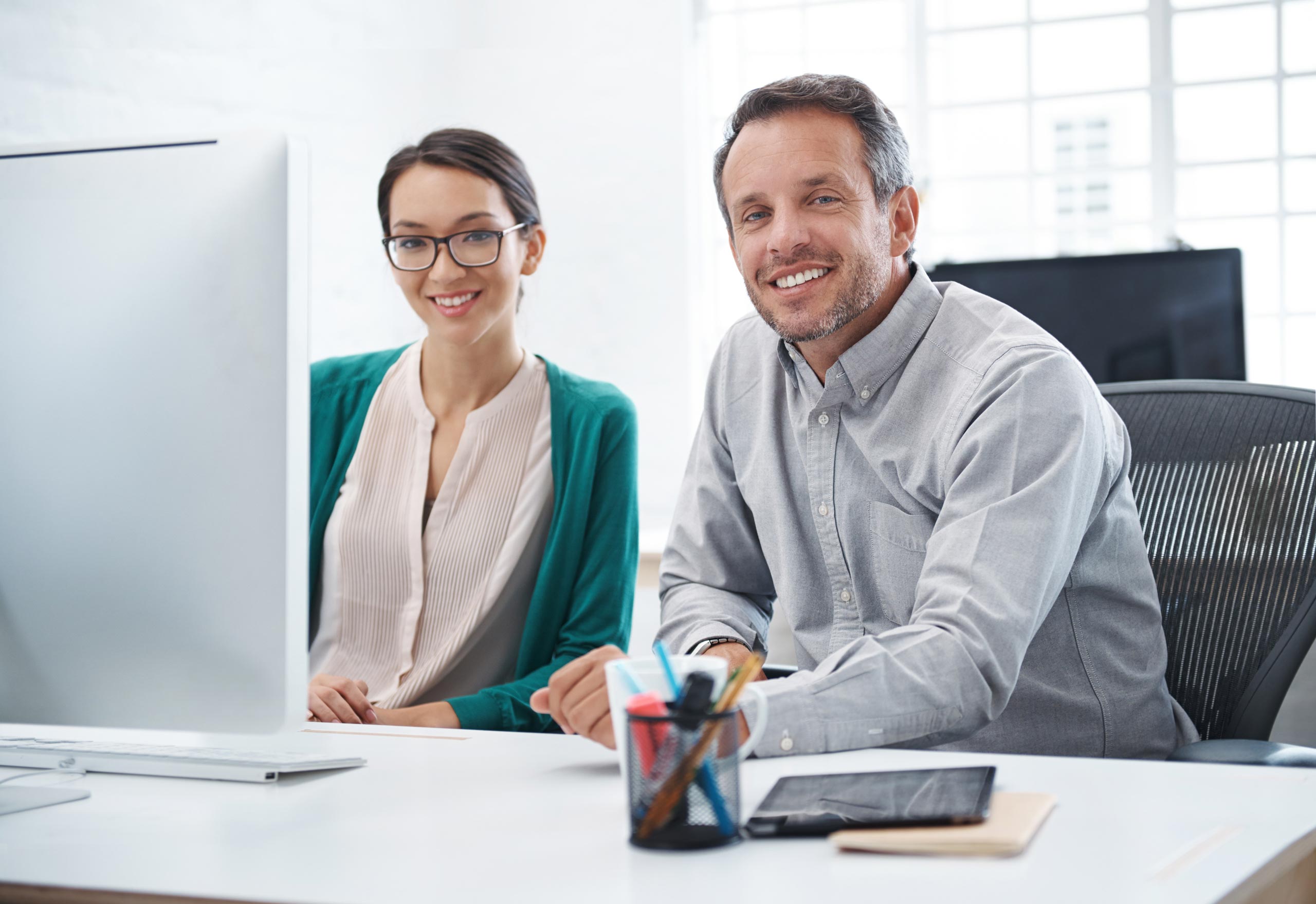 Young woman and man sitting in front of an iMac, smiling to the camera
