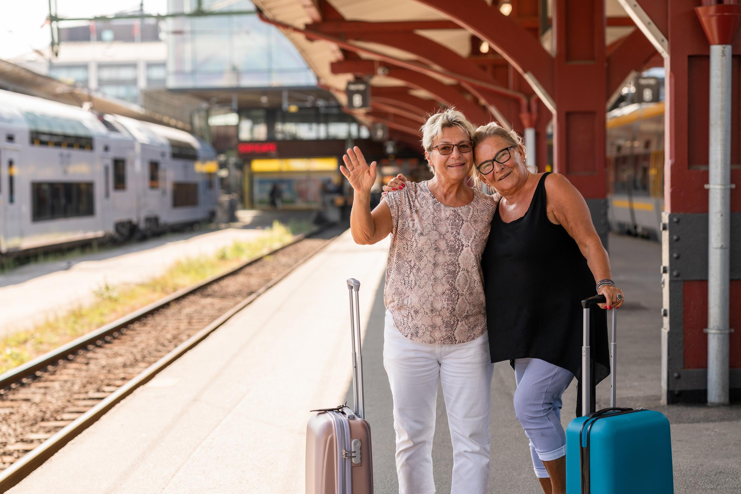 Two happy women with suitcases on a railway platform