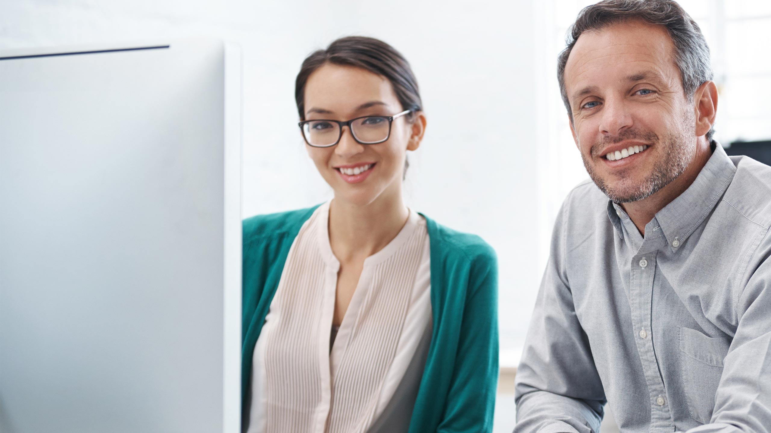 Happy young woman and man sitting behind an iMac