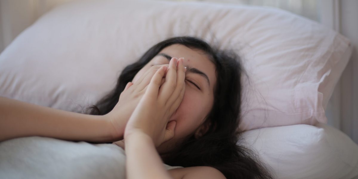 Woman lying on bed covering her face with her hands